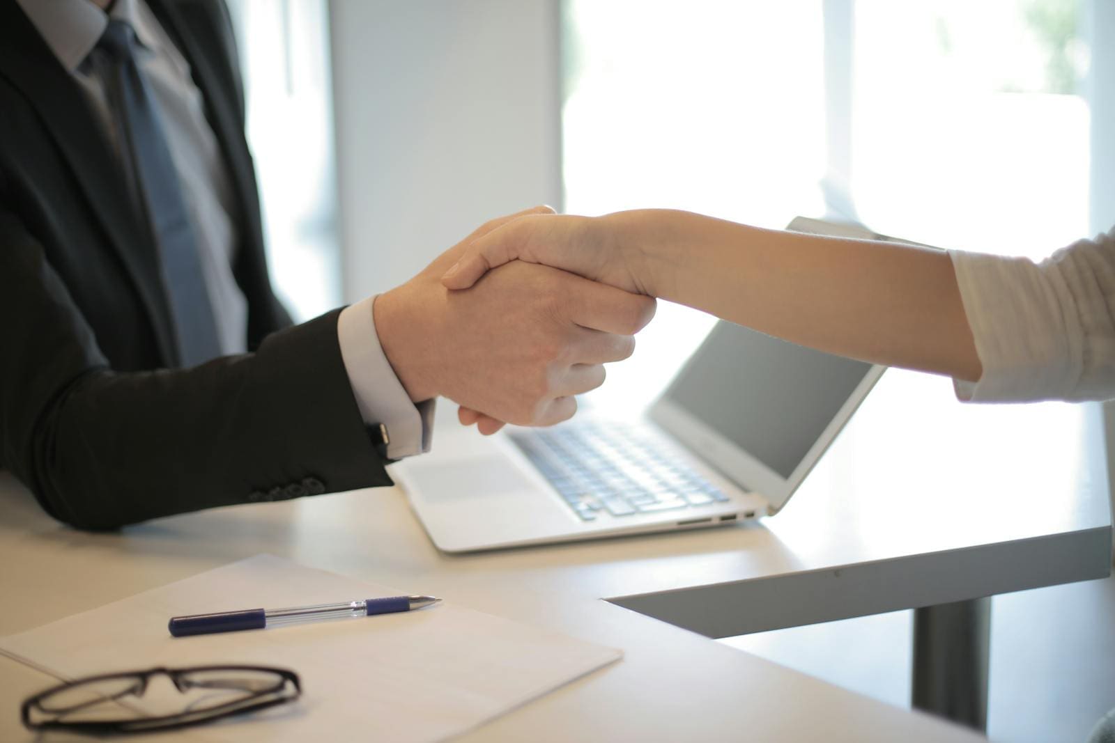 Close-up of a professional handshake over a laptop during a financial services strategy meeting.
